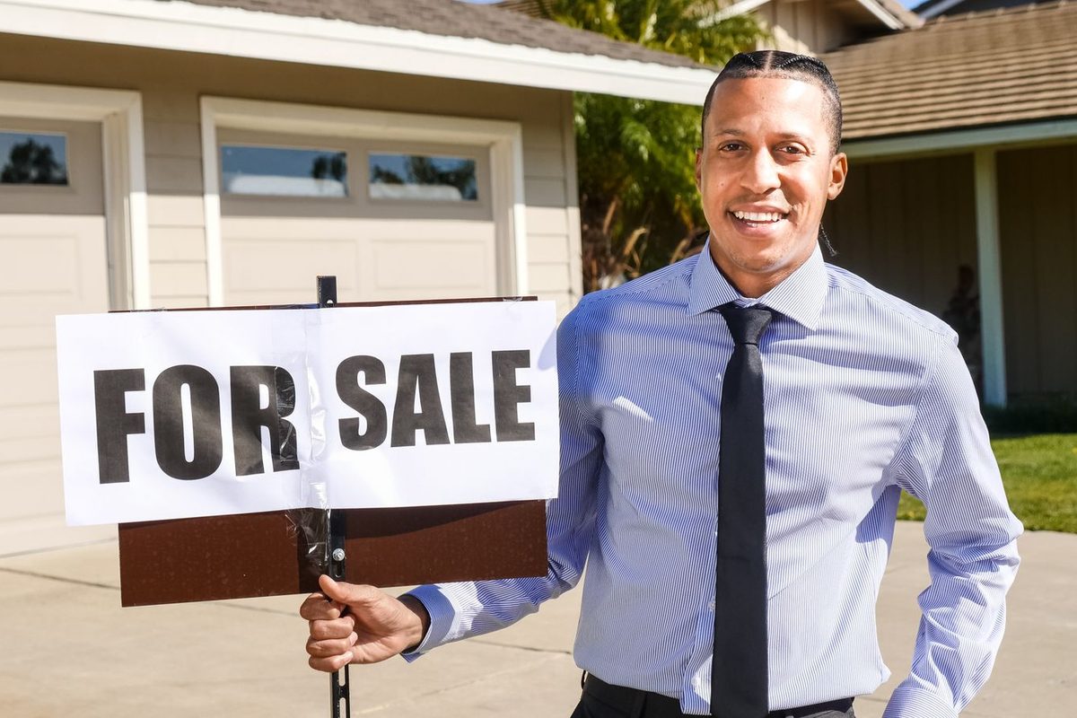 Agent immobilier tenant un panneau devant une maison