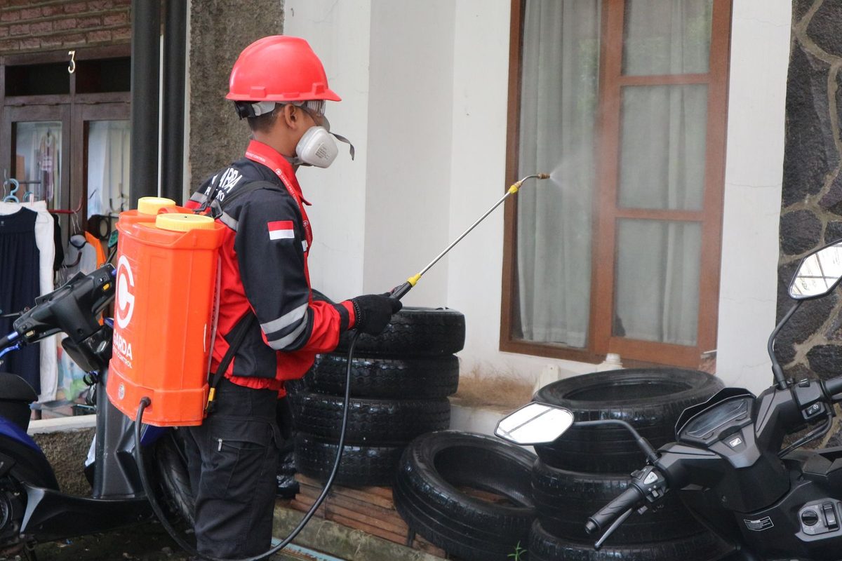 Technicien en équipement de protection pulvérisant un traitement le long d'un bâtiment