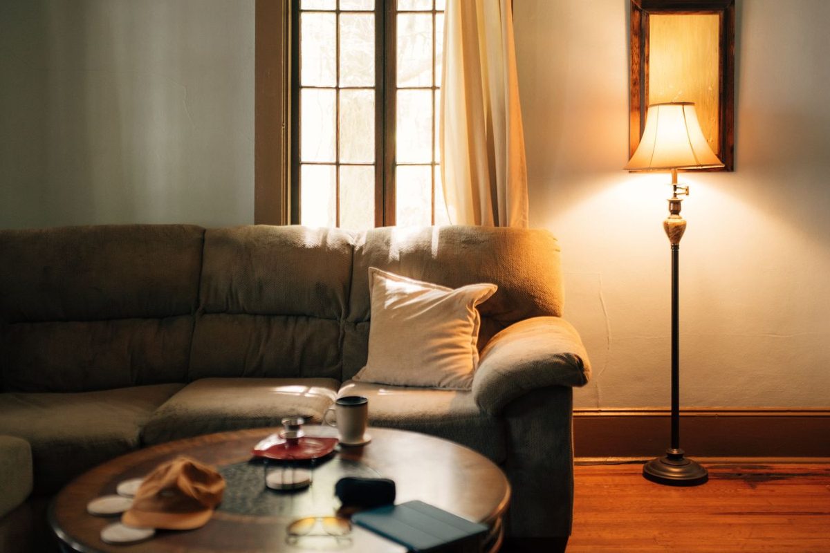 Lampadaire allumé à côté d'un canapé, dans un salon en lumière chaude