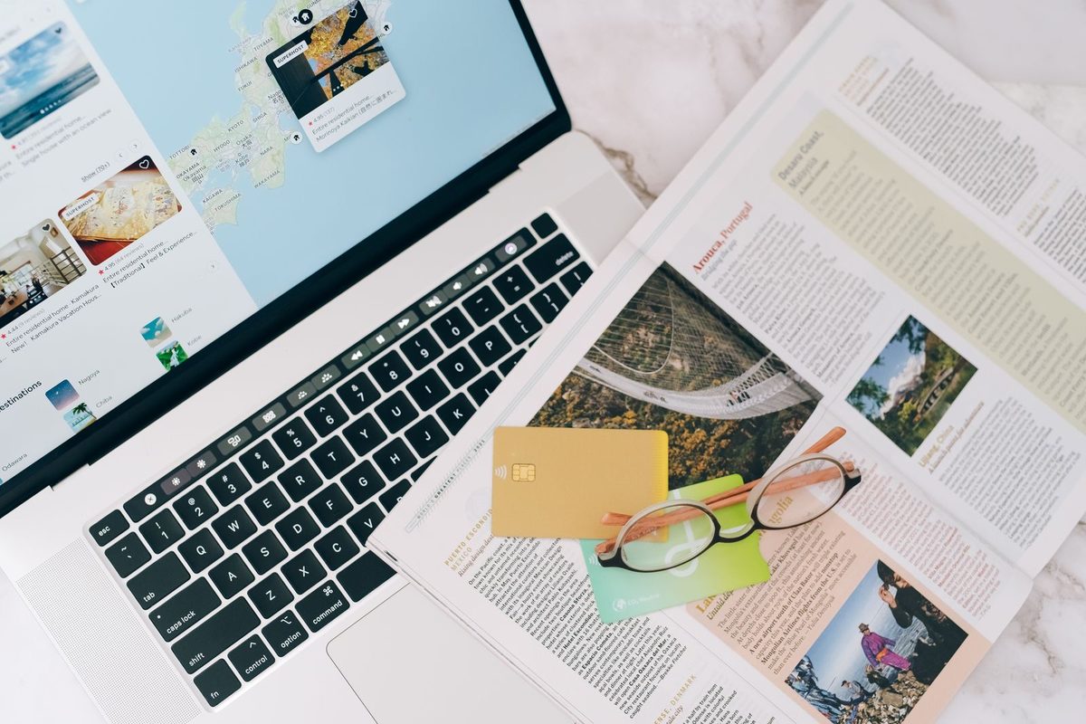 Ordinateur portable ouvert sur un site de voyage, entouré de cartes et de brochures