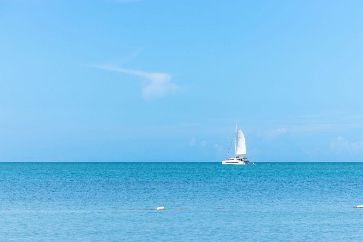 Voilier blanc naviguant seul sur une mer turquoise sous un ciel dégagé