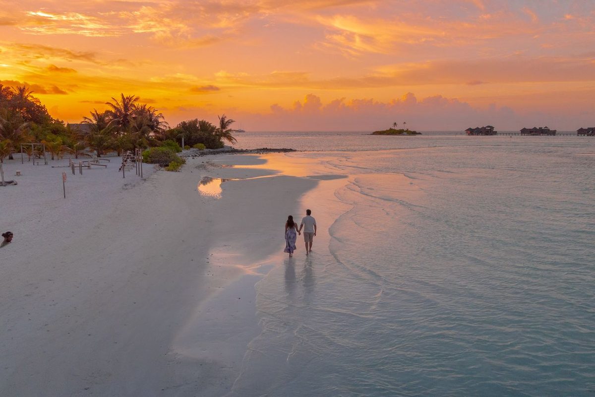 Couple marchant au bord de l'eau sur une plage déserte au coucher du soleil