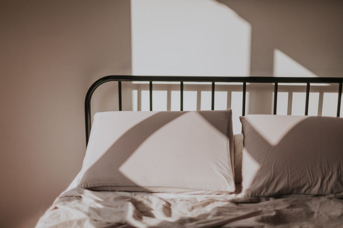 Lit défait au cadre métallique, draps clairs éclairés par la fenêtre