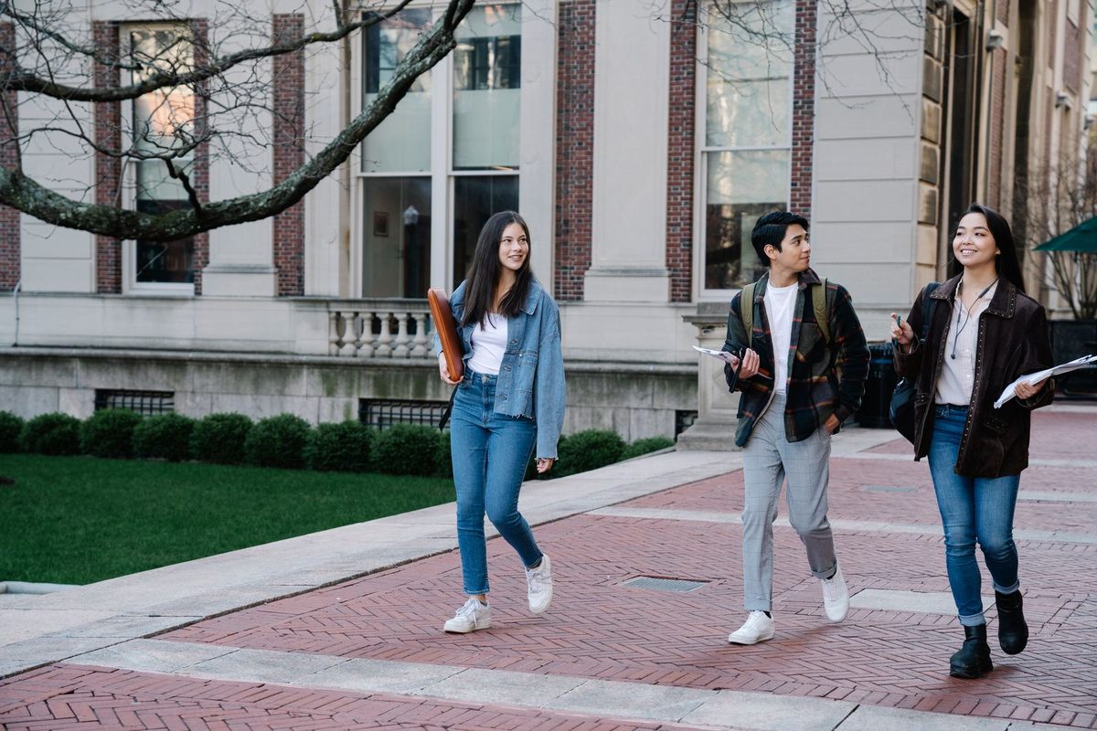 Trois étudiants marchant côte à côte devant un bâtiment universitaire américain