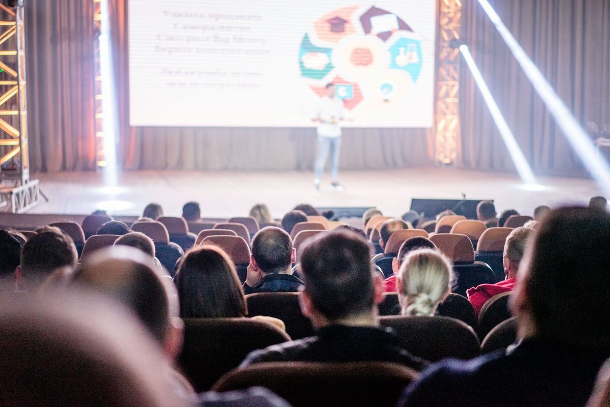Salle comble écoutant une intervention, écran de présentation allumé