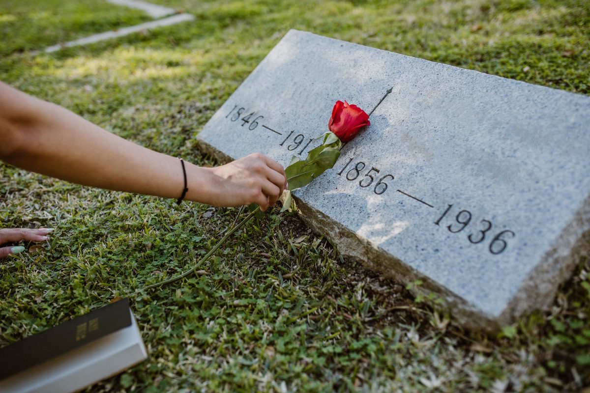 Main déposant une rose rouge sur une pierre tombale