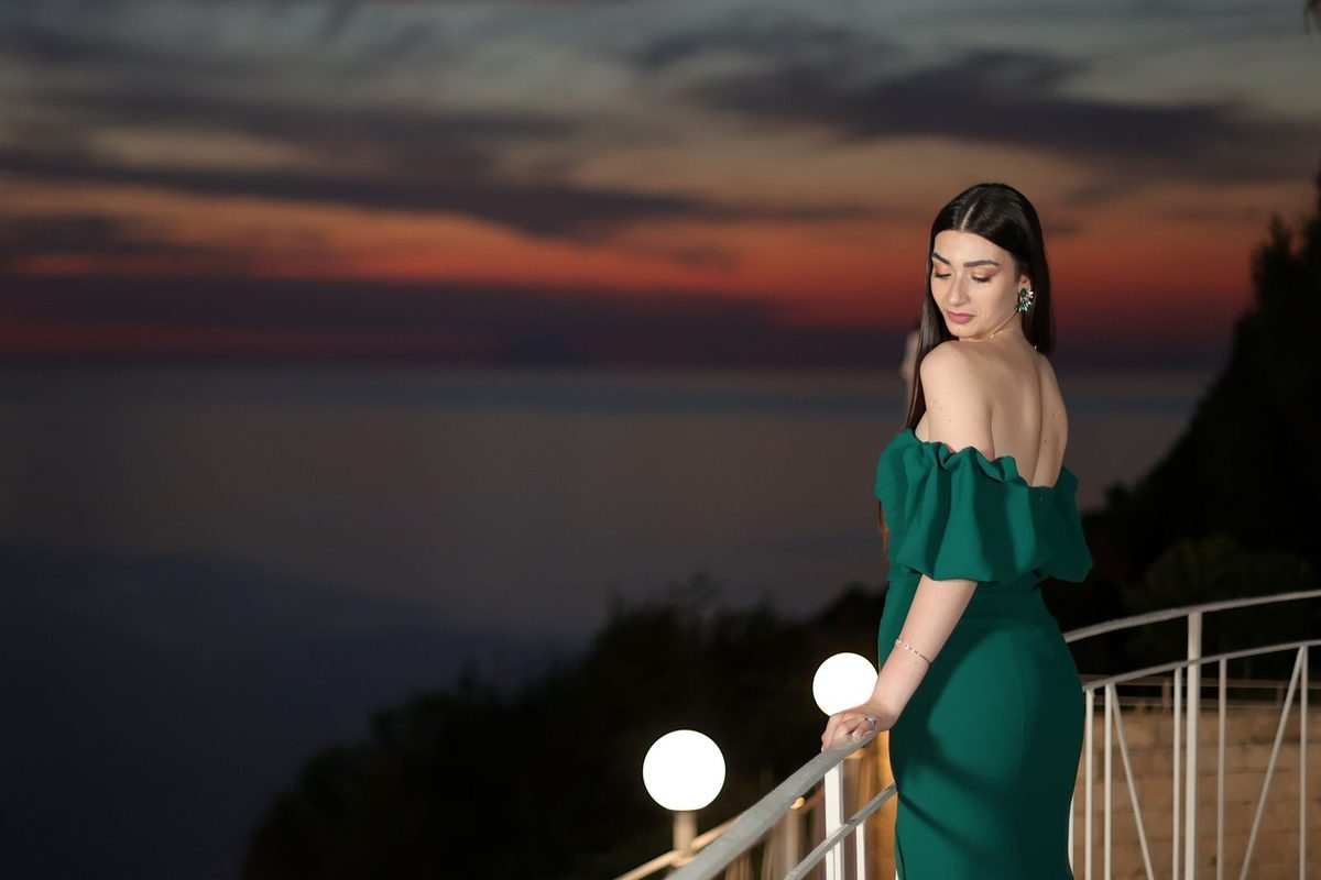 Femme en robe verte sur un balcon, au coucher du soleil