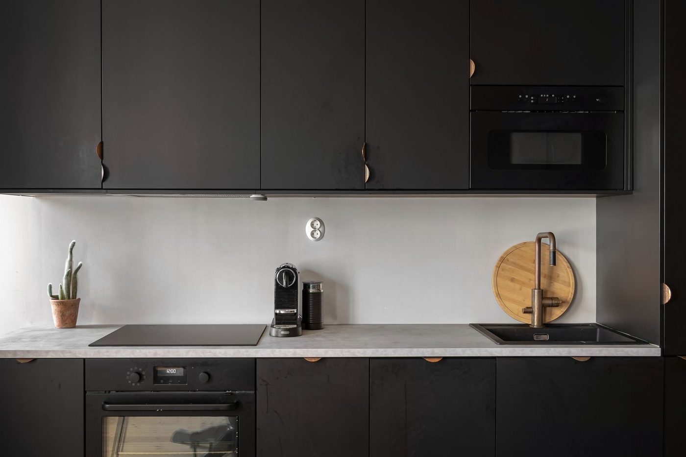 Cuisine aux façades noires mates avec plan de travail et crédence clairs