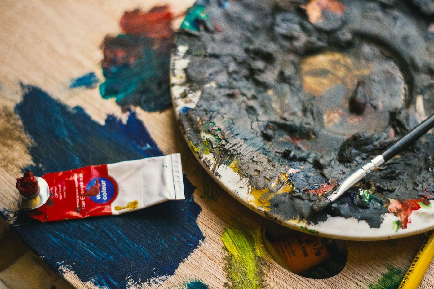 Palette de peintre chargée de rouges sombres et tube de peinture posé à côté